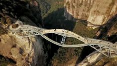 an aerial view of people walking on a bridge over a canyon in the middle of mountains