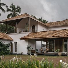 a large white house with brown tiled roofing and palm trees in the back ground