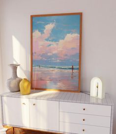 a painting sitting on top of a white dresser next to a vase and yellow vase