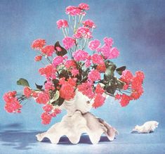 a vase filled with pink flowers sitting on top of a blue table next to a shell