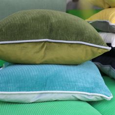 three pillows stacked on top of each other in front of a green chair with blue and yellow cushions