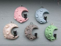 four different colored cat shaped pendants on a white surface with black cats sitting in the crescent