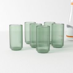 four green glass tumblers sitting next to each other on a white surface with a bottle in the background