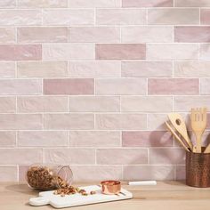 a wooden table topped with utensils next to a pink brick wall covered in white tiles