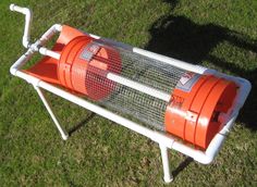 an orange bird cage sitting on top of a grass covered field next to a metal pipe