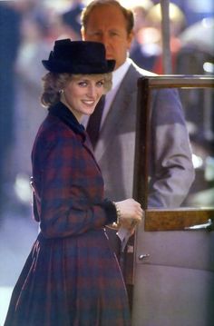 a woman in a plaid coat and hat standing next to a man wearing a suit