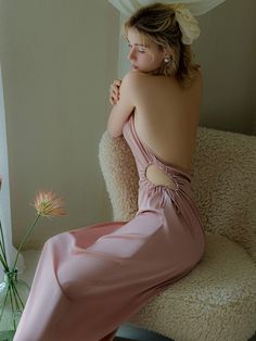 a woman in a pink dress sitting on a chair next to a vase with flowers