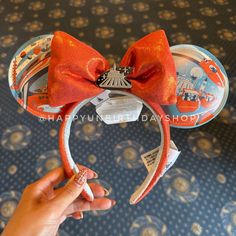 a person holding up a minnie mouse ears headband with an orange bow on it