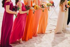 a group of women standing next to each other on top of a sandy beach holding bouquets