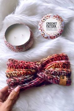 a hand holding a knitted headband next to a candle and some other items