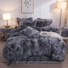 a bed with grey fur and pillows on top of it in front of a white wall