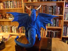 a blue dragon figurine sitting on top of a wooden table in front of bookshelves