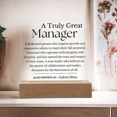 there is a quote on the shelf next to a vase with flowers in it that reads, a truly great manager