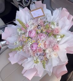 a bouquet of pink and white flowers sitting on top of a car seat in front of a steering wheel