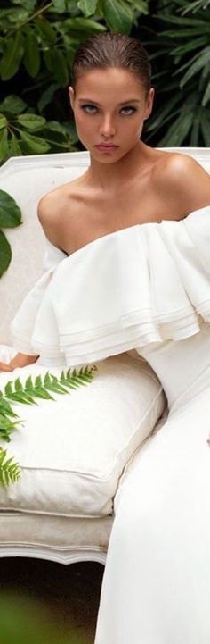 a woman sitting on top of a white couch in front of green plants and greenery