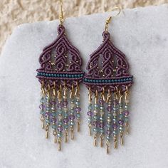 a pair of purple and blue beaded earrings on top of a white rock with beads hanging from it