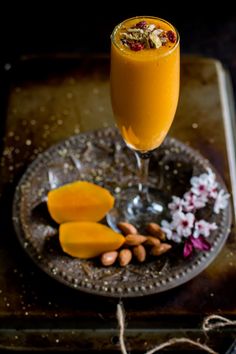 a glass filled with orange juice sitting on top of a plate next to almonds