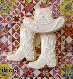 two decorated cookies with cowboy boots on them sitting on a quilted tablecloth background