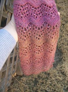 someone is holding up a pink and purple knitted shawl