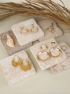 four pieces of jewelry sitting on top of marble coasters next to some dried grass