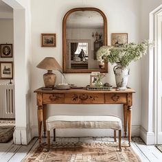 a wooden table topped with a mirror and a vase filled with flowers next to a bench