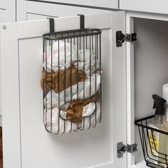 a cage hanging on the side of a kitchen cabinet filled with towels and other items