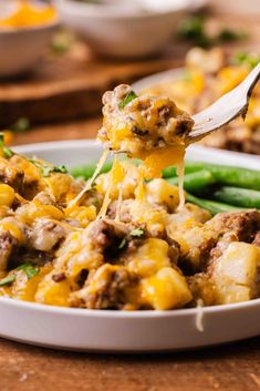 a spoon full of food with cheese on it and green beans in the foreground