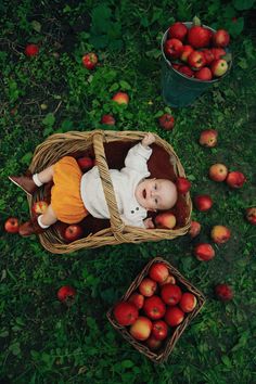 a baby laying in a basket next to some baskets filled with apples on the ground