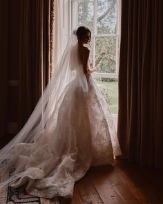 a woman standing in front of a window wearing a wedding dress with a long veil