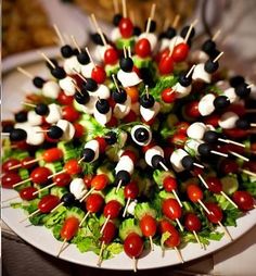 an arrangement of skewered tomatoes and black olives arranged on a white plate