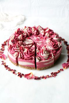 a cake with pink frosting and rose petals around it on a white tablecloth