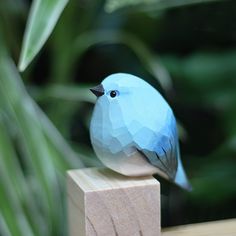 a small blue bird sitting on top of a wooden block in front of some plants