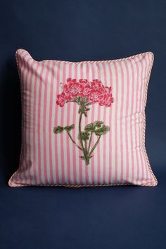 a pink and white striped pillow with flowers embroidered on the front, sitting against a blue background