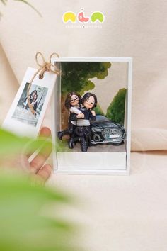 a hand holding a card with an image of two people sitting on top of a car