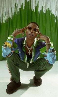 a man in green pants and sunglasses is posing for a photo with his hands on his head