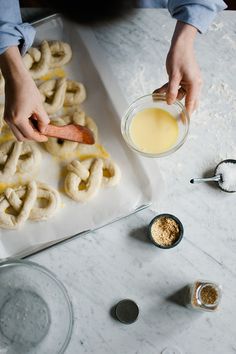 a person is making homemade pretzels on a white table with bowls and spoons