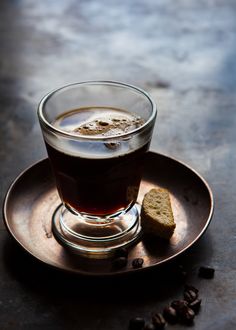 a glass cup filled with liquid next to pieces of bread on a metal saucer