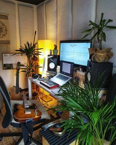 a computer desk with a guitar, keyboard and monitor on it next to a potted plant