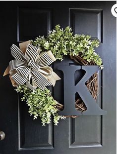 a wreath with the letter k is hanging on a black door and it's decorated with greenery