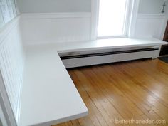 a white bench sitting on top of a hard wood floor next to a large window