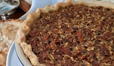 two pies sitting on top of white plates next to each other with pecans in them