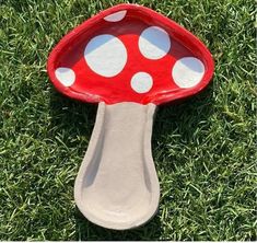 a red and white mushroom shaped dish sitting on top of green grass in the sun