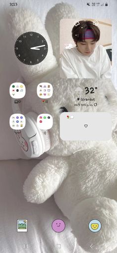 a white teddy bear sitting on top of a bed next to a clock and other items