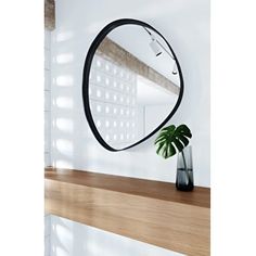 a mirror sitting on top of a wooden shelf next to a vase with a plant in it