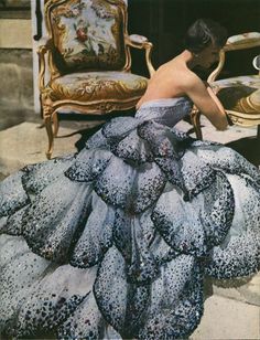 a woman in a dress sitting on the ground next to a chair and table with chairs around it