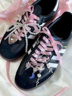 two pairs of black shoes with pink bows and pearls on the laces are sitting on a white sheet