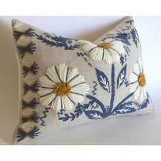 a blue and white pillow with daisies on the front, sitting on a white surface