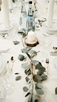 the table is set with silverware, candles and greenery for an elegant dinner