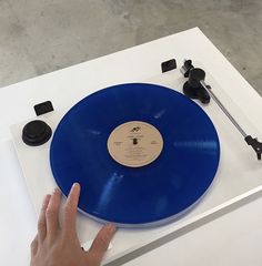 a person touching a blue record on top of a white table next to a black object