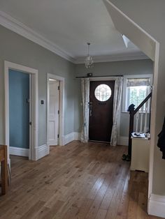 an empty living room with wood floors and white trim on the door, windows, and curtains